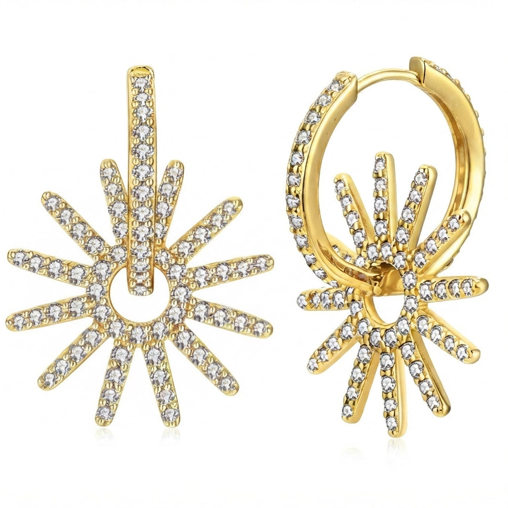 A pair of gold huggie hoop earrings featuring a sunburst design paved with clear cubic zirconia stones, displayed on a clean white background.