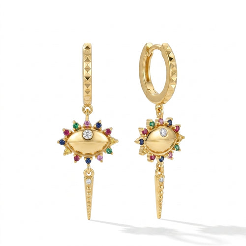 A pair of gold huggie hoop earrings with dangling evil eye charms, decorated with colorful gemstones and a central clear crystal, shown on a white background.