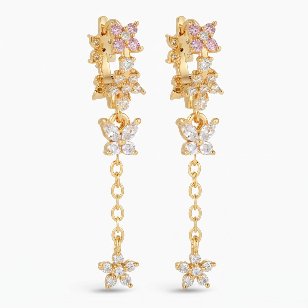 A pair of gold dangle earrings featuring butterfly and flower motifs, embellished with clear cubic zirconia stones and pink gemstones, set against a plain white background.