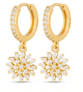 A pair of gold hoop earrings with pavé-set clear stones along the front and dangling snowflake-shaped charms, each adorned with small clear stones, shown on a white background.