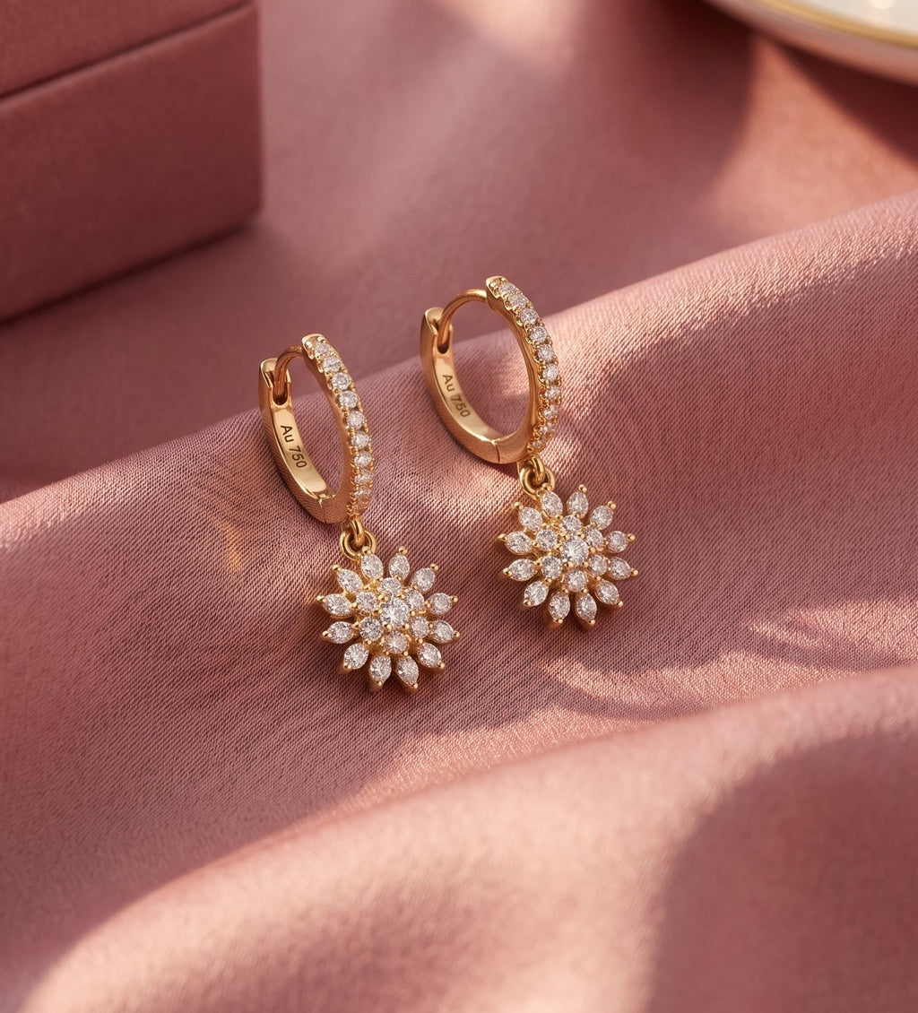 A pair of gold huggie hoop earrings with small pavé diamond clusters at the ends, styled on draped dusty pink satin fabric next to a matching pink jewelry box.