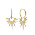 A pair of gold huggie hoop earrings with dangling sunburst charms, embellished with pavé-set clear cubic zirconia stones, shown on a solid white background.