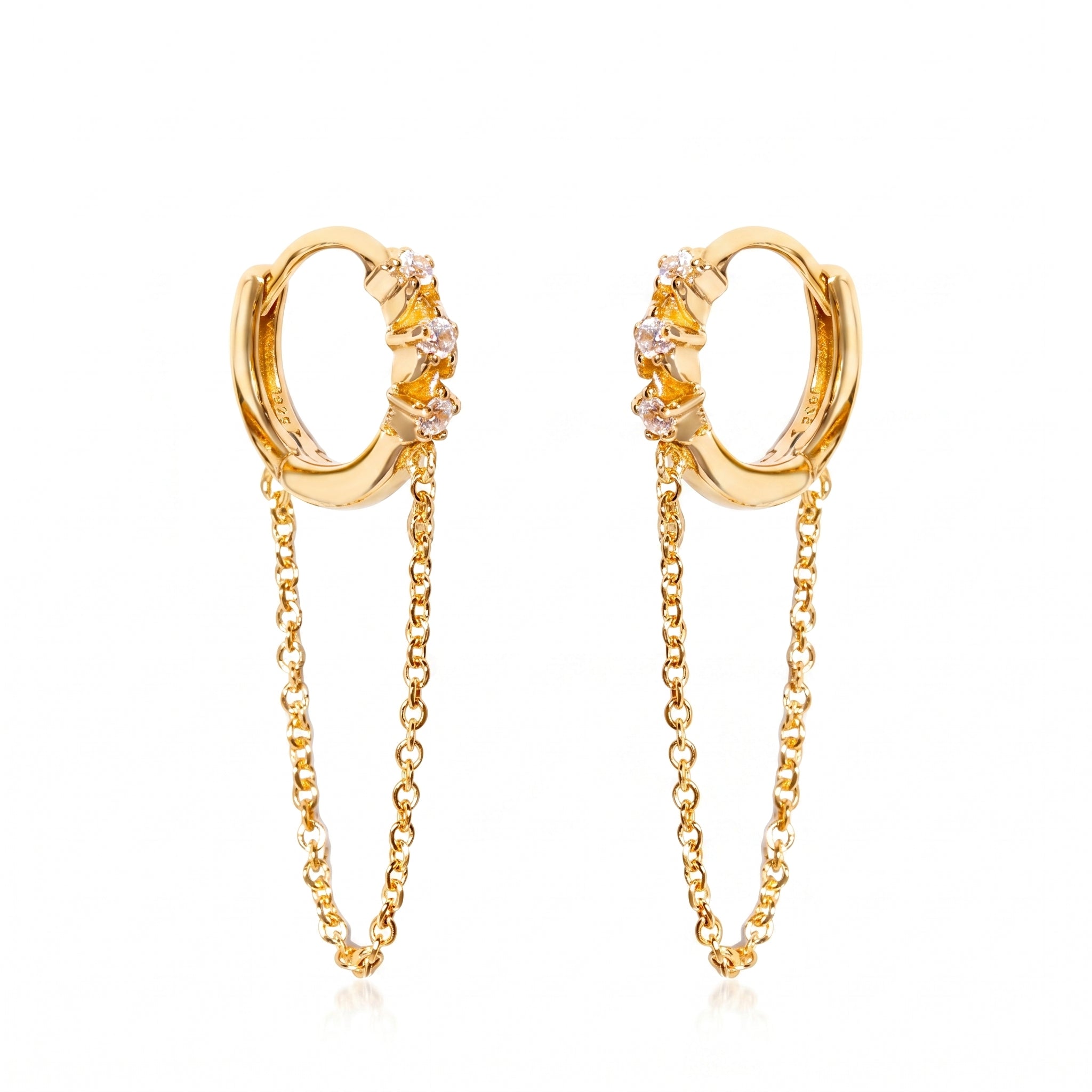 A pair of gold huggie hoop earrings with small clear gemstones and dangling chain accents, shown on a plain white background.